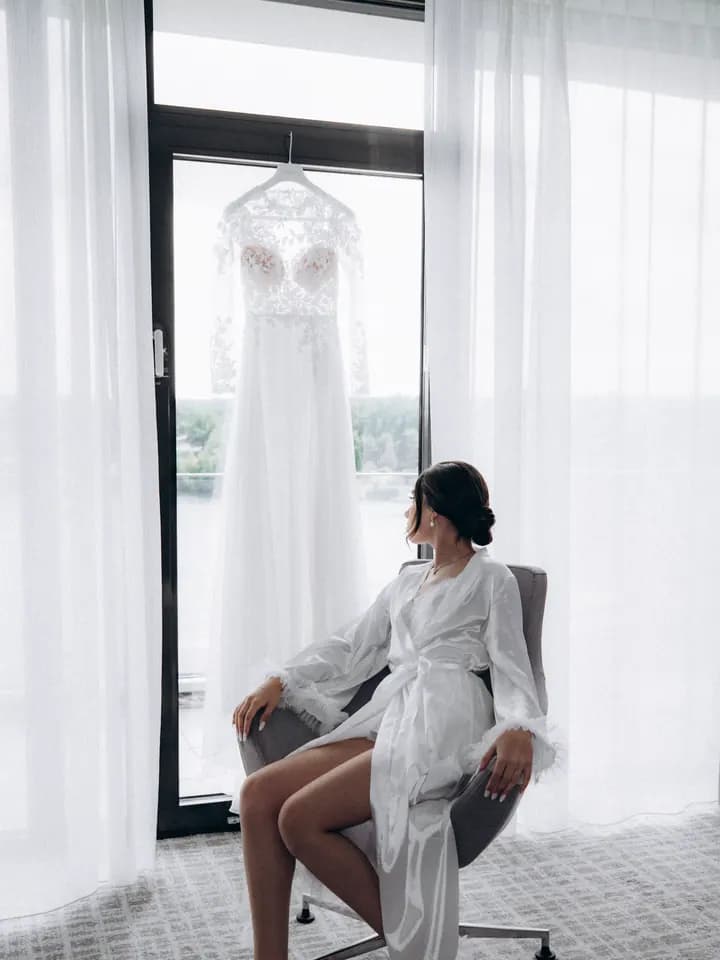Getting Ready: Braut im Morgenmantel, das Kleid hängt am Fenster